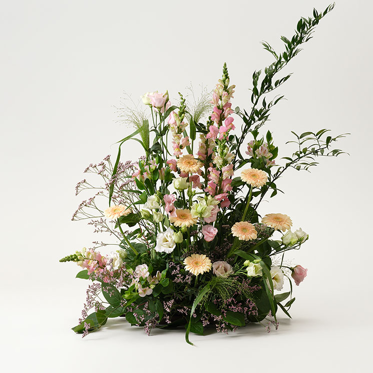 Hög begravningsdekoration, med germini, prärieklocka, alstroemeria och lejongap. Ljusa rosa och aprikosa färgtoner. Skicka med ett blommogram från Interflora direkt till begravningen!